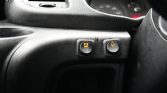 Close-up of a car dashboard showing two black buttons with yellow illuminated icons: the left button has a bell warning symbol, the right button has a triangle warning symbol.