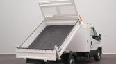 White utility dump truck with its bed raised, ready to unload material in a neutral indoor space.