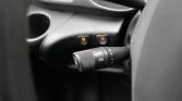 Close-up of a car steering column stalk showing OFF and ON, with plus and minus markings, and small orange indicator lights in the background indicating aux controls are active.