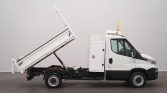 White utility truck with a raised tilting dump bed and hydraulic support, ready to unload materials in a workshop setting.