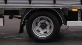 Close-up of a truck wheel: silver rim, black tire, with a small orange side marker light nearby on the truck body.