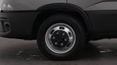 Close-up of a vehicle's front wheel and tire on a gray van, showing the hubcap and wheel arch.