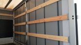 Interior of an empty cargo trailer with horizontal wooden load-rails secured to gray walls for securing freight