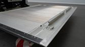 Close-up of a silver aluminum loading ramp with a textured surface and edge latch on a concrete floor.