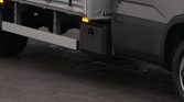 Close-up of a large dark-gray truck shows a long horizontal underrun protection bar extending from the side near the ground beneath the cargo area.