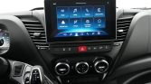 Center touchscreen on the car dashboard shows app icons (Radio, Media, Phone, Apple CarPlay) above climate controls and hazard button, in a modern interior view. Informative: describes function and elements.