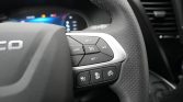 Close-up of steering wheel with cruise control and media buttons on a modern car dashboard edge. Discreet perforated leather visible on the wheel.