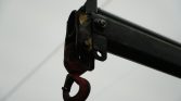 Close-up of a rusty red lifting hook attached to a black metal crane arm, with bolts and a bracket against a pale sky background.