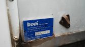 Close-up of a blue metal nameplate on a gray surface, showing company info, address in the Netherlands, and the serial number Z1028395 with rust along the bottom edge.