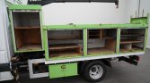 Green mobile workshop cabinet mounted on a truck, with multiple open shelves and drawers for tools and parts.