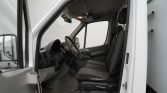 Front interior of a white van showing the driver's seat, steering wheel, and front passenger seat with worn upholstery.