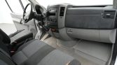 Interior of a grey cargo van: steering wheel, center console, dashboard, and front seats visible from the passenger side door.