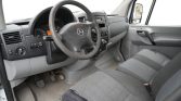 Interior of a Mercedes van: steering wheel, dashboard, and front seats, with worn driver seat fabric and pedals visible.