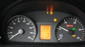 Car dashboard with a speedometer up to 180 km/h, central digital display, and warning lights illuminated at the top of the cluster.