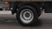 Close-up of a truck wheel: silver steel rim with lug nuts, black tire, and an orange side marker light above the wheel well .