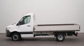 White flatbed truck shown in profile from the left side in a studio setting; cargo bed is empty.
