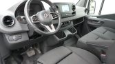 Interior view of a Mercedes van cabin showing steering wheel, dashboard with touchscreen, center console, and two front seats.