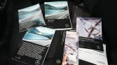 Several Mercedes-Benz vehicle brochures and manuals spread on a car seat, featuring road scenes and the Mercedes logo (Sprinter and warranty materials).