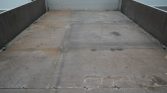 Empty flatbed trailer with a weathered metal floor and rust stains, viewed from the back toward the cab.