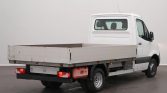 Rear three-quarter view of a white Mercedes Sprinter flatbed truck with an open cargo bed and wooden sides, parked indoors