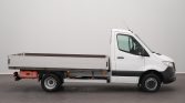 Side view of a white cab-over flatbed truck with an empty cargo bed in profile.