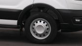 Close-up of a white van's front wheel with a silver hubcap and black tire rim visible under the fender.