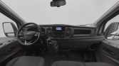 Interior of a vehicle cabin: steering wheel, manual gear shifter, and central dashboard with a screen and controls.