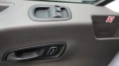 Car door interior: window switch panel, door handle, and lock/unlock button visible on textured black panel.