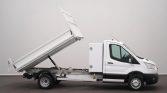 White dump truck shown from the side with its cargo bed raised, ready to unload, supported by a hydraulic piston.