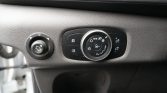 Car headlight control cluster: central round dial with headlight and fog icons and side buttons for brightness; left small dial for other controls. (Close-up)