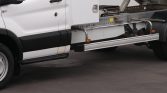 White utility truck side view showing a metal step rail and chassis with a hydraulic mechanism and storage box behind the cab
