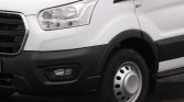 Front-left view of a white van showing the headlight, grille, and wheel with a silver hubcap on a black bumper edge.