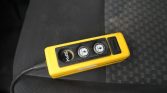 Yellow handheld remote with three circular buttons and a connected cord, resting on a dark car seat upholstery.
