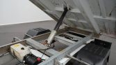 Tilt-bed trailer showing hydraulic lift ram raising the metal bed on a utility trailer
