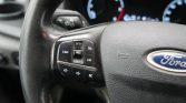 Close-up of a car steering wheel with cruise control buttons on the left and the Ford emblem visible on the right shelf of the wheel panel