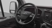 Interior of a vehicle cabin featuring a left-hand drive steering wheel with Ford logo and gear shift visible to the right of the wheel