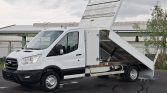 White utility/dump truck with hydraulic bed raised, ready to dump material on a paved lot.