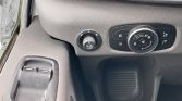 Close-up of a car's driver-side controls: circular headlight/fog light dial next to window switches on a textured gray dashboard.