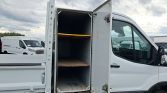 White utility van with its rear storage compartment open, revealing two wooden shelves inside.