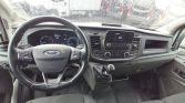 Interior view of a Ford van dashboard: steering wheel, manual gearshift, and center console on a rainy day
