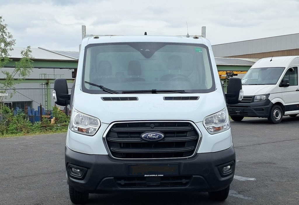 White Ford transit-style van viewed head-on in a parking lot; prominent grille and front bumper with Ford emblem.