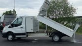 White utility truck with a hydraulic tilt bed raised for unloading on a paved lot