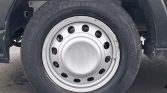 Front wheel of a Ford van with a silver steel rim and hubcap showing the Ford logo, tire mounted