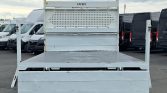 Rear view of a light gray flatbed truck with a perforated headboard and 'CALVET' branding, parked among vans in a lot