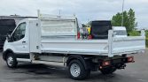White flatbed truck with open cargo bed and metal side rails, parked in a lot (rear and side view).
