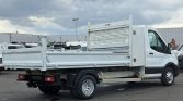 Rear three-quarter view of a white utility truck with an open flatbed and metal storage cage, parked in a lot.
