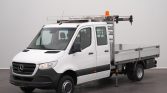 White Mercedes-Benz utility flatbed truck with ladder rack and orange beacon in a studio setting.