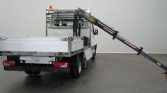 White flatbed tow truck with an extended hydraulic crane reaching to the right in a showroom setting