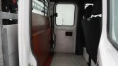 Interior of a white cargo van with a diamond-plate metal floor, brown side panel, and front seats visible through the open doorway at the back of the cabin.