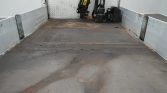 Empty industrial trailer bed with metal side rails, showing rust stains and a tucked-away machine at the far end.